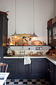 L-shaped kitchen counter and chequered floor below pendant lamps in kitchen of period building