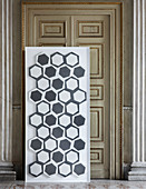 Moderne Fliesen mit grau-weißen Mustern auf Platte vor antiker Tür