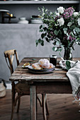A bouquet and pastries on a rustic wooden table in a country kitchen