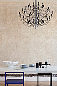 Modern chandelier above dining table in front of patinated wall