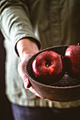 Hände halten Holzschale mit zwei roten glänzenden Äpfeln