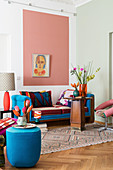 Pouffe and couch providing accents of blue, wooden table and pink field on wall in living room