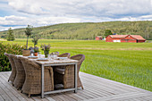 Table and wicker chairs on deck with view of fields and woods