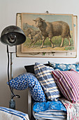 Old poster of sheep above bench with blue-patterned cushions
