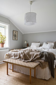 Double bed and bedroom bench in bedroom with pale grey walls