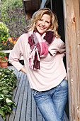 A blonde woman wearing a pink blouse, a thick scarf and jeans