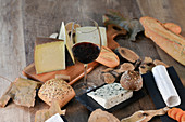 Käseplatte mit Brötchen, Baguette, Rotwein und Herbstblättern auf Holztisch
