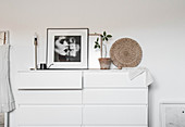 Weiße Schubladenschrank mit schwarz-weißer Fotografie, Tischlampe und Zimmerpflanze