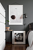 Moderne Kunst an grauer Wand über Nachttisch und schwarz-weiße Fotografie im Schlafzimmer