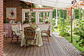 Tisch und Rattanstühle auf ländlicher Terrase mit Sonnenschutz im Garten