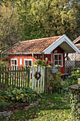 Red summerhouse behind fence in late summer garden