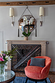 Coral-red easy chair in front of fireplace with decorative metal screen