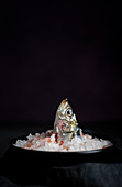 Head of salted mackerel sticking out from plate full of salt on black background