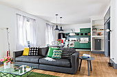 Sofa, dining table and kitchen area in bright, open-plan interior with green and grey accents