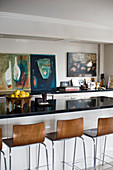 Barstools at breakfast bar of open-plan kitchen decorated with abstract paintings on walls