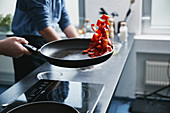 A cook tossing pepper pieces in a pan