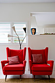 Two red armchairs with scatter cushions in front of white wall