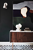 Sideboard with sculpture and modern art next to wall lamp