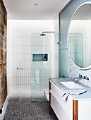 Runder Spiegel über Waschtisch mit Marmorplatte im Badezimmer mit Duschbereich