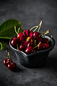 Ripe cherries with red flower in bowl at grey table indoors