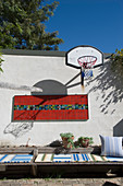 Individuell gestalteter Innenhof mit Basketballkorb, Mosaikwandbild und flachen Holzsitzmöbeln