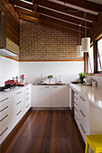 U-shaped kitchen with white cabinets and dark wooden floor below sloping wooden ceiling