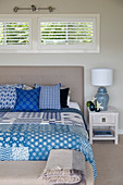 Blue-and-white patchwork quilt and scatter cushions on bed with upholstered headboard