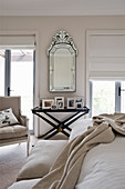 Mirror on wall and pictures on black tray table in beige bedroom