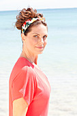 Brunette woman wearing colourful headband and red, short-sleeved blouse on beach