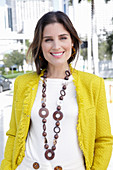 A young woman wearing a chunky necklace, a white jumper and a yellow bouclé jacket