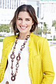 A young woman wearing a chunky necklace, a white jumper and a yellow bouclé jacket