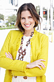 A young woman wearing a chunky necklace, a white jumper and a yellow bouclé jacket