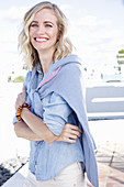 A blonde woman wearing a denim shirt with a jumper over her shoulders