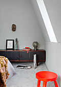 Orangefarbener Hocker und Lowboard im Schlafzimmer mit leichter Dachschräge