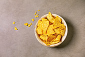 Tortilla nachos corn chips in ceramic bowl over brown texture background