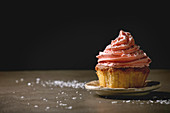 Ein Cupcake mit rosa Buttercreme-Frosting vor schwarzem Hintergrund