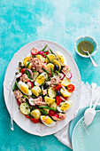 Salad with potatoes, tuna, boiled eggs, radish, cherry tomatoes, onions, black olives and green beans, dressed with herbed vinaigrette