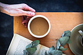 Woman's hand holding a coffee cup on a wooden table with a book