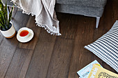 Teacup, blanket, cushion and magazines on dark wooden floor