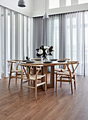 Designerstühle am runden Holztisch vor Fensterfronten mit Gardinen