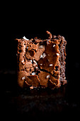 A brownie with flakes of sea salt against a black background