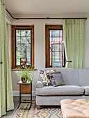 Pale grey sofa set and side table in front of windows with green curtains