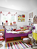 Kinderbett mit Kissen und Steppdecke, Wimpelkette über Fenster und Wanddeko im Mädchenzimmer