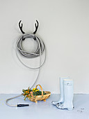 Garden hose coiled on antler-shaped, wall-mounted rack, basket and wellington boots