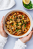 Woman holding a bowl of vegan oyster mushroom soup on a light background
