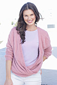 Junge Frau mit langen Haaren in fliederfarbenem T-Shirt und Wickel-Pullover