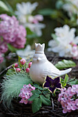 Ceramic bird amongst lilac flowers, petunias, apple blossom and feather