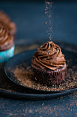 Schokoladenraspel rieseln auf veganen Schokoladen-Cupcake