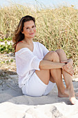 A woman with long hair wearing a white summer jumper and white shorts