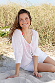 A woman with long hair wearing a white summer jumper and white shorts